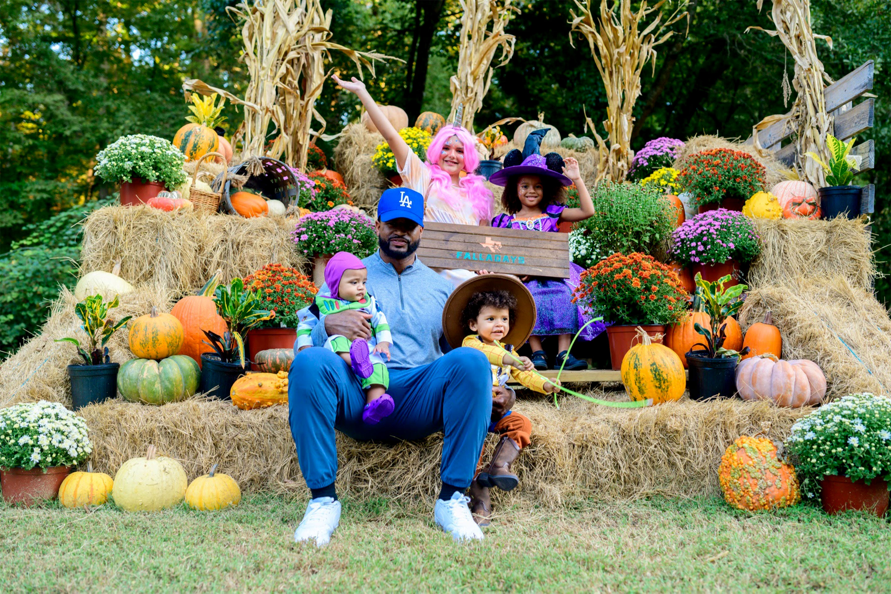 A man, two young toddlers, and two young girls sit on a festive stack of hay bails.