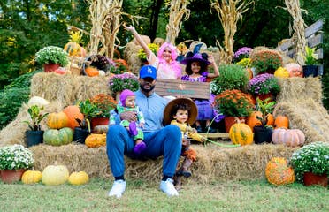 A man, two young toddlers, and two young girls sit on a festive stack of hay bails.