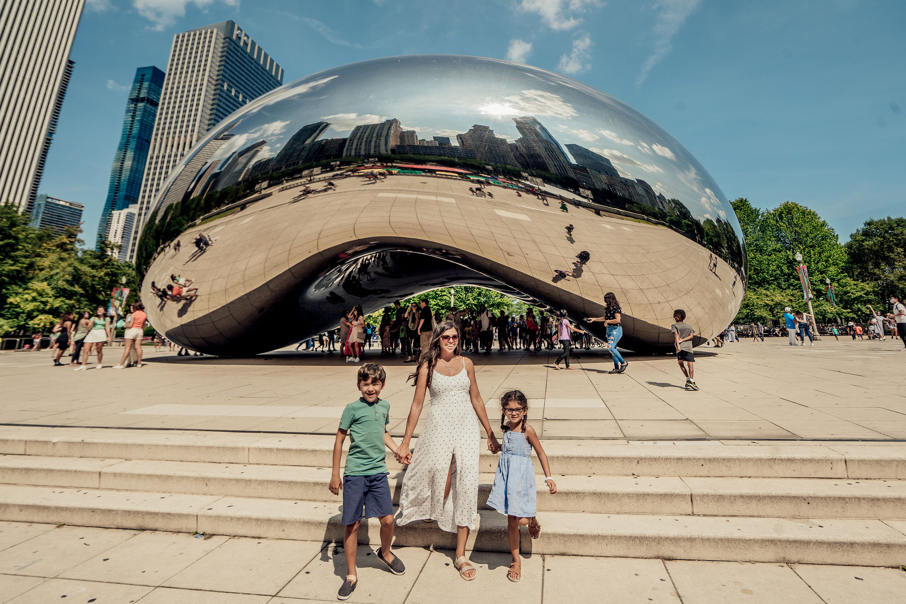 A woman (middle) holding a young boy (left) and young girls (right) hand at cloud gate in Chicago.