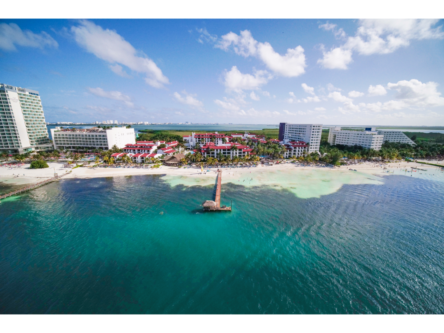 Aerial view of beachfront resorts with turquoise ocean and sandy shore.