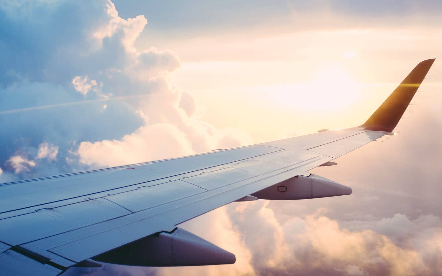 The wing of an airplane floats through clouds and a sunset.