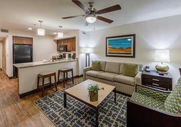 Living room with couch and accent chair with kitchen in background in a one-bedroom villa at Scottsdale Resort