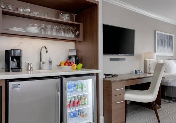 Modern hotel room featuring compact kitchenette area, desk workspace, and stocked mini-fridge.