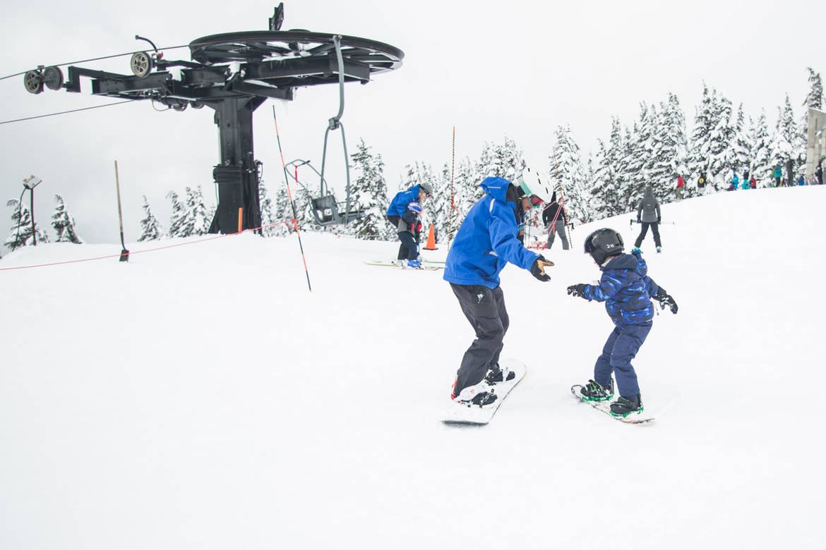 A man and child are learning to snowboard near a ski lift.