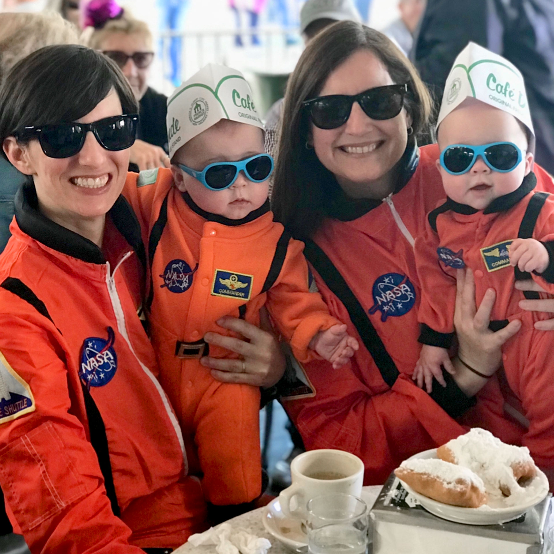 Featured Contributor, Catherine Karas, and her family enjoy beignets indoors dressed in orange astronaut suits.