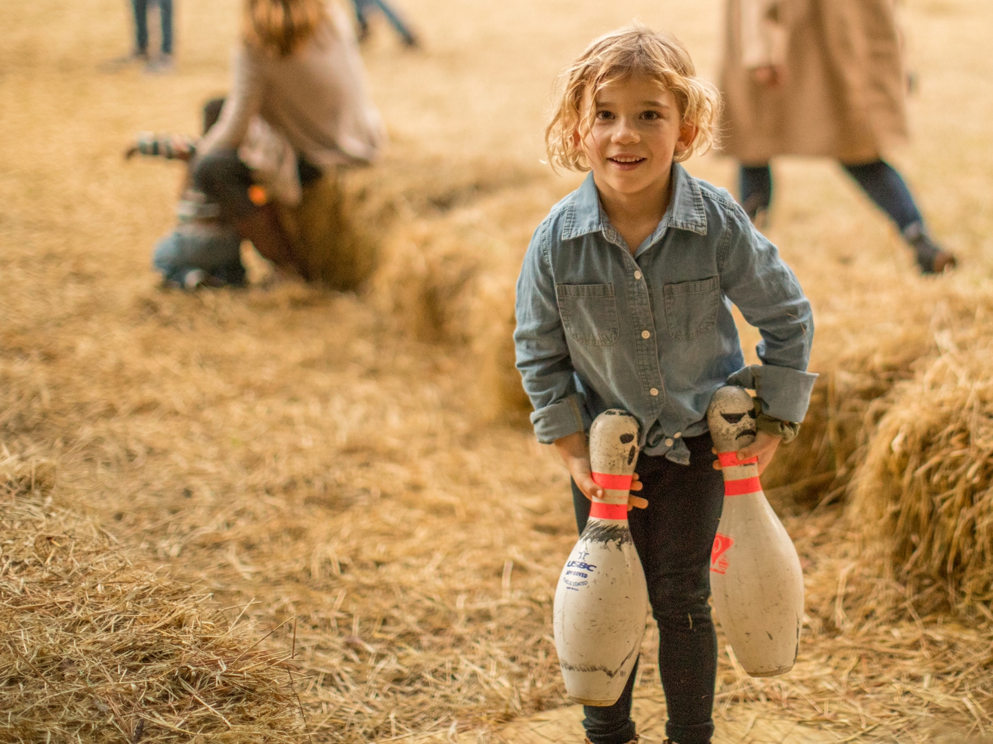 Child carrying bowling pins in hay.
