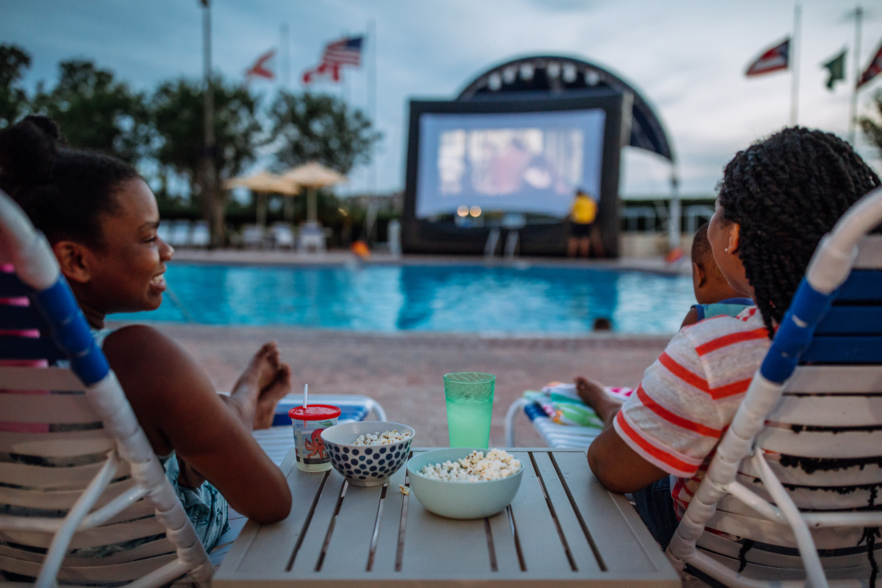 Krystin Godfrey (right) and daughter Sabria (left) enjoy watching a summer outdoor movie near the edge of the pool on a large inflatable screen.