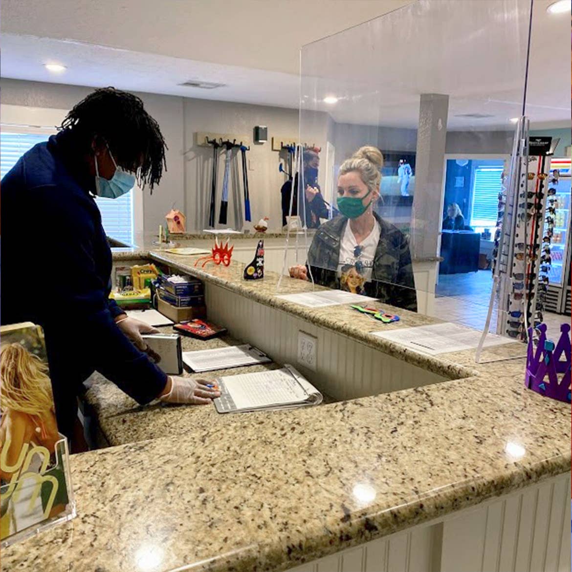 A Team Member assists Amanda with mini-golf equipment rentals while both wear a mask behind plexiglass at our Galveston Beach Resort.