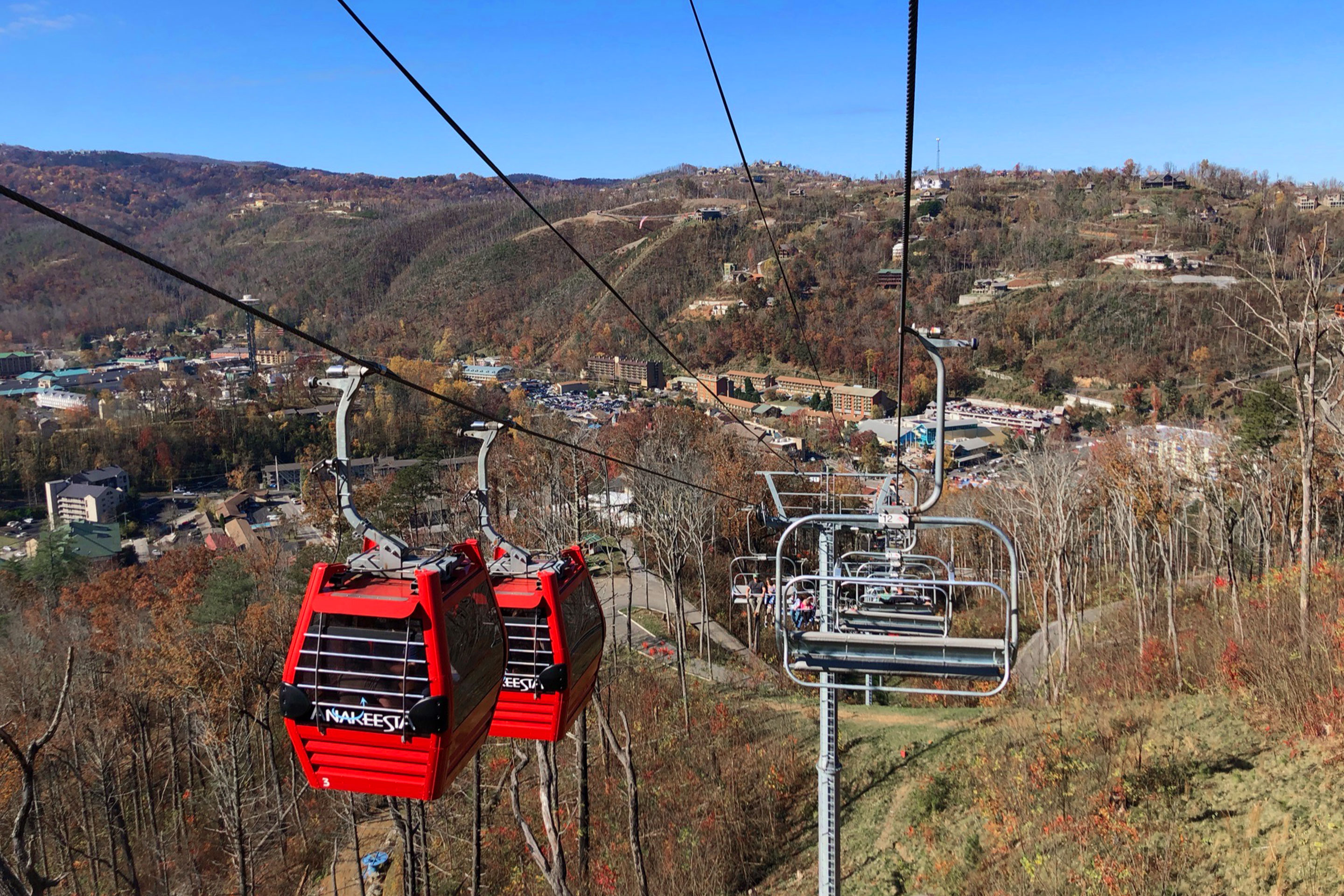 Two read gondolas (left) ascend while chair lifts (right) descend above the forested mountains of Tennesse.