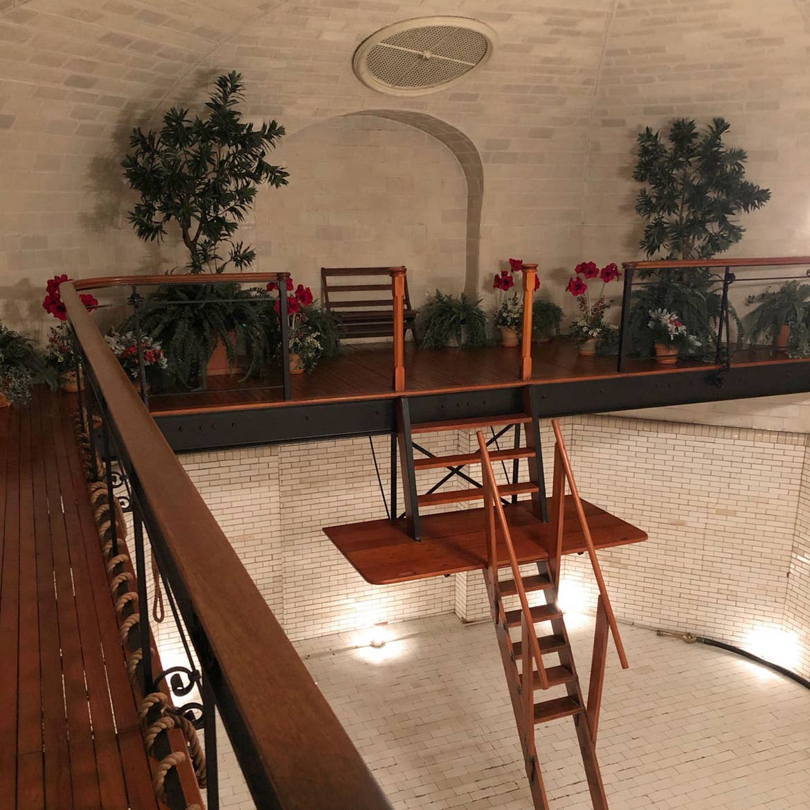 The empty indoor pool of the Biltmore Estate in the evening with an elaborate wooden ladder for swimmers surrounded by lush greenery.