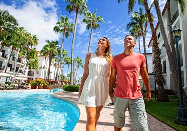 A couple walking beside an outdoor pool surrounded by palm trees at The Royal Cancun in Cancun, Mexico.