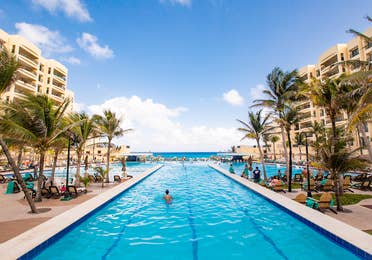 A guest floating in an outdoor pool that is surrounded by palm trees and looks onto ocean at Royal Sands Resort in Mexico.