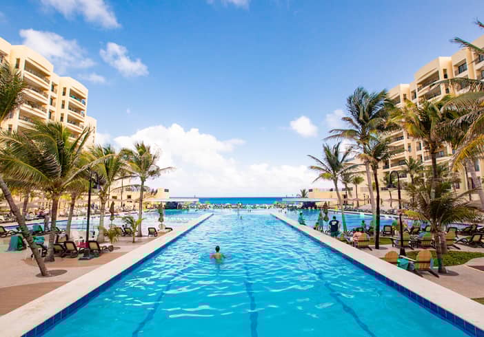 A guest floating in an outdoor pool that is surrounded by palm trees and looks onto ocean at Royal Sands Resort in Mexico.