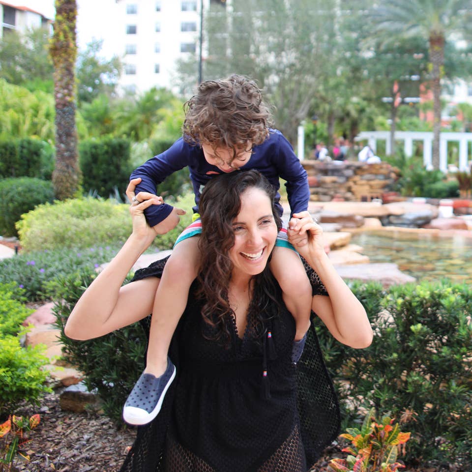 Woman laughing and carrying a child on her shoulders.
