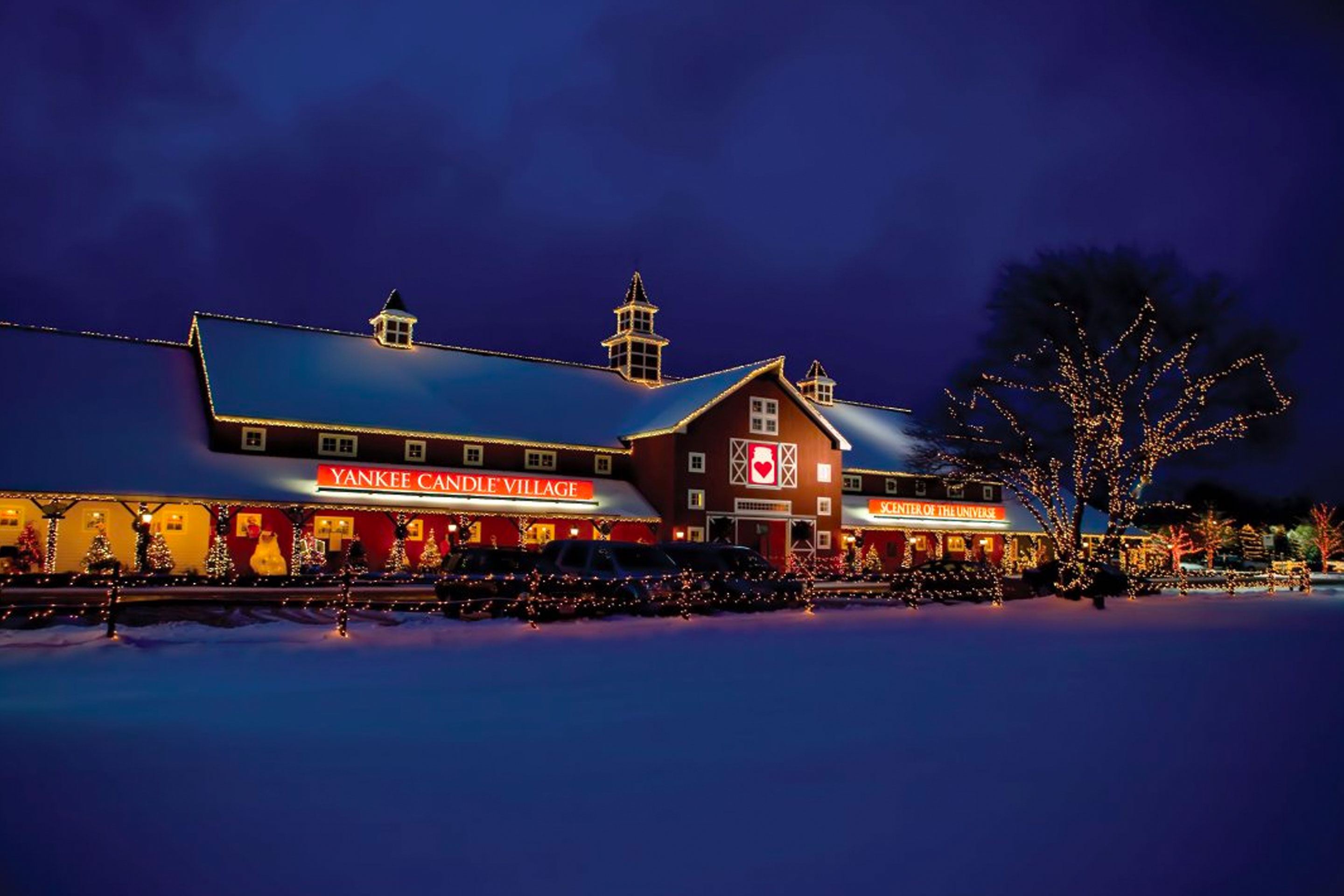 The exterior of the Yankee Candle Village storefront can be seen covered in white snow at night.