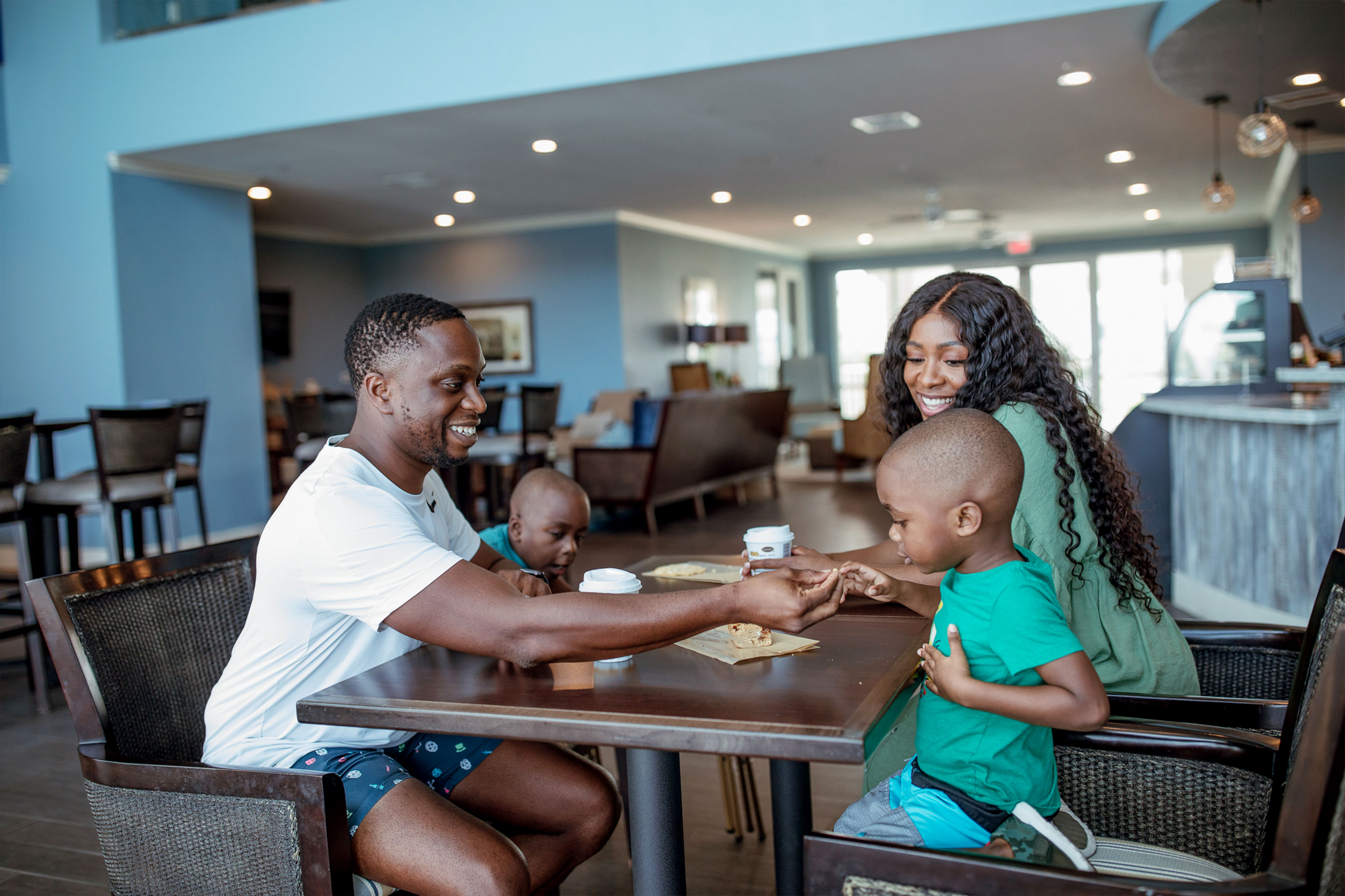 A man, a woman and two young boys enjoy muffins at an indoor table.
