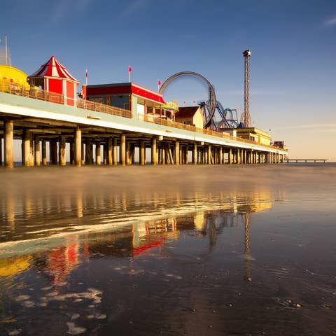 View of the Galveston Pleasure Pier at twilight showing a smooth ocean and carnival rides in motion.