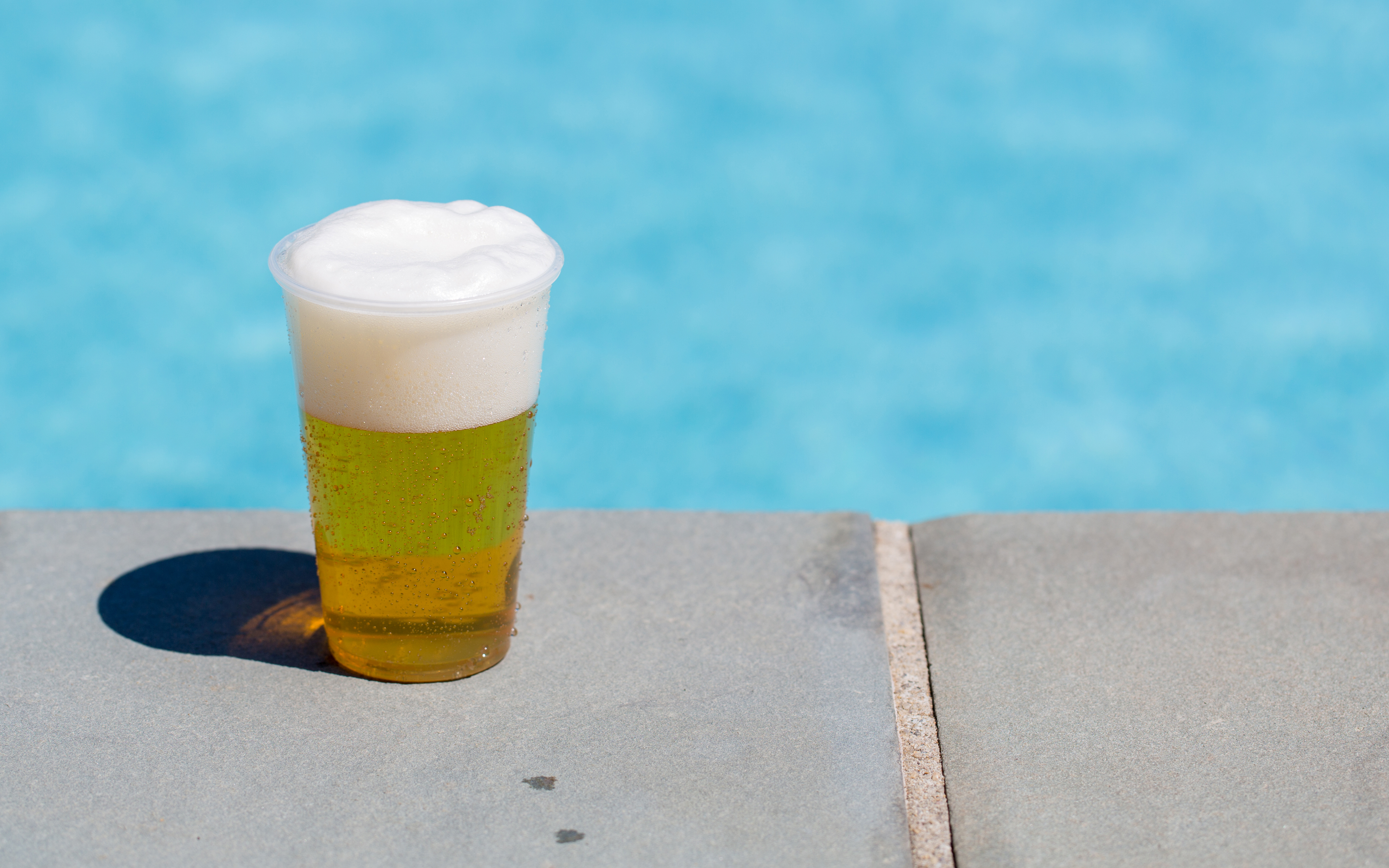Glass of beer by an outdoor pool.