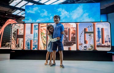 A young girl (left) embraces a young boy (right) in front of a sign that reads, 'Chicago.'