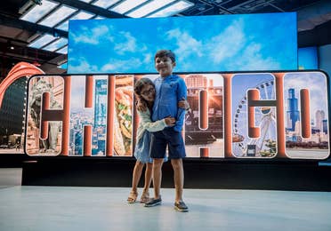 A young girl (left) embraces a young boy (right) in front of a sign that reads, 'Chicago.'
