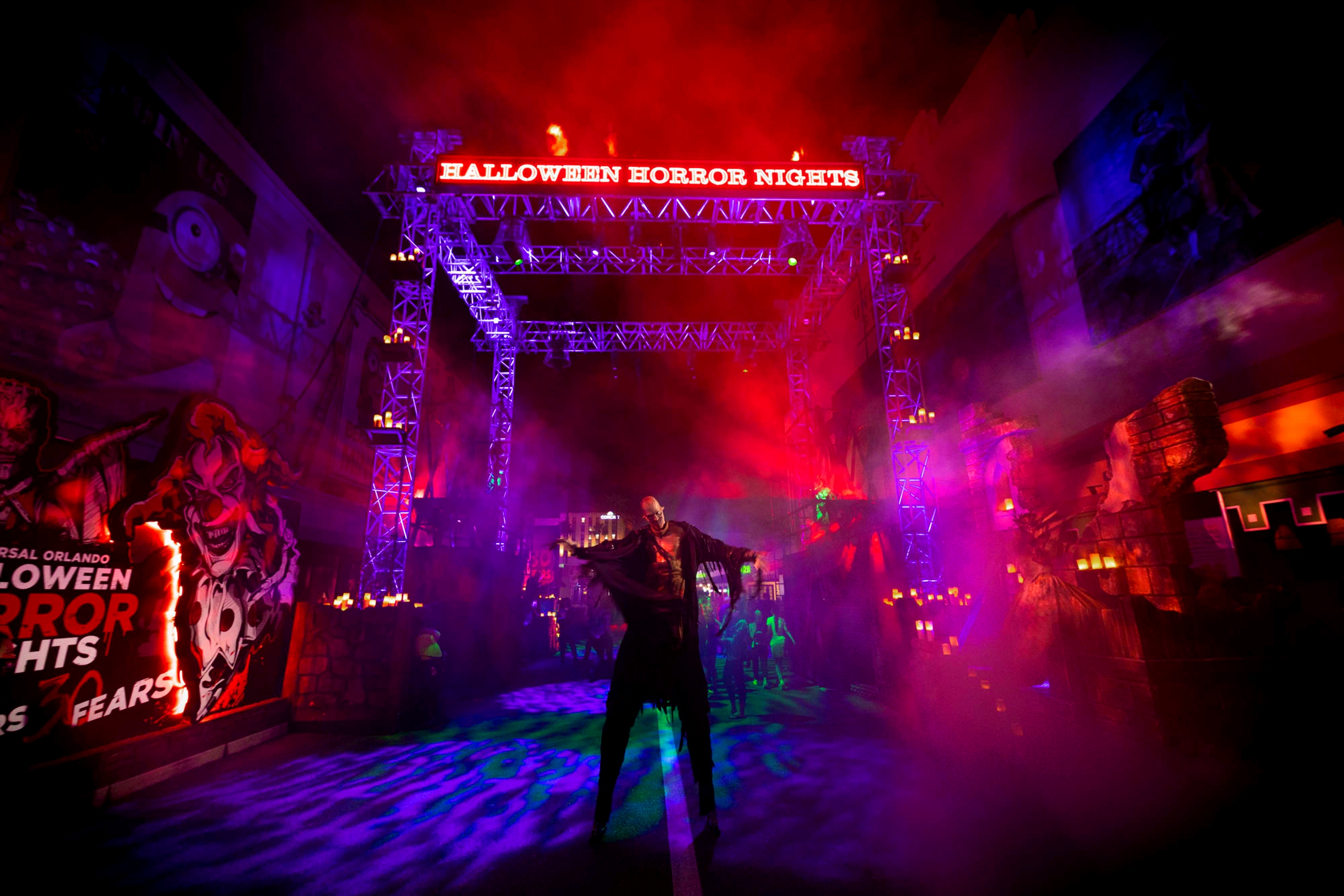 A tall figure stands under a scaffold with lighting at night.