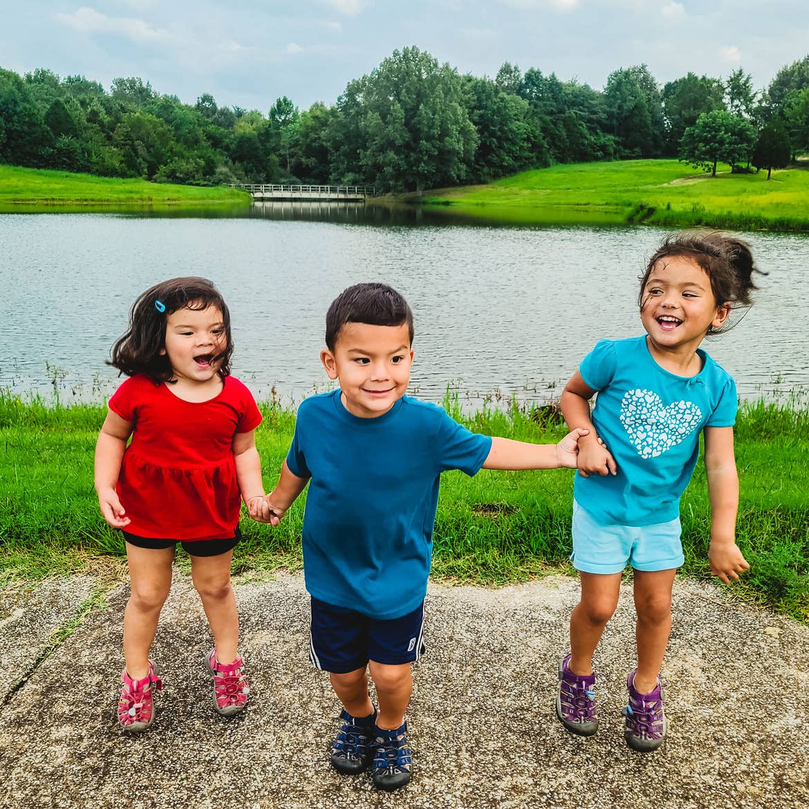 Angelica's three children smile happily in front of a pond in their RV park.