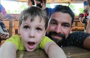 A young boy (left) and man (right) stand in an attraction queue surrounded by guests in safety masks and mouse ears.
