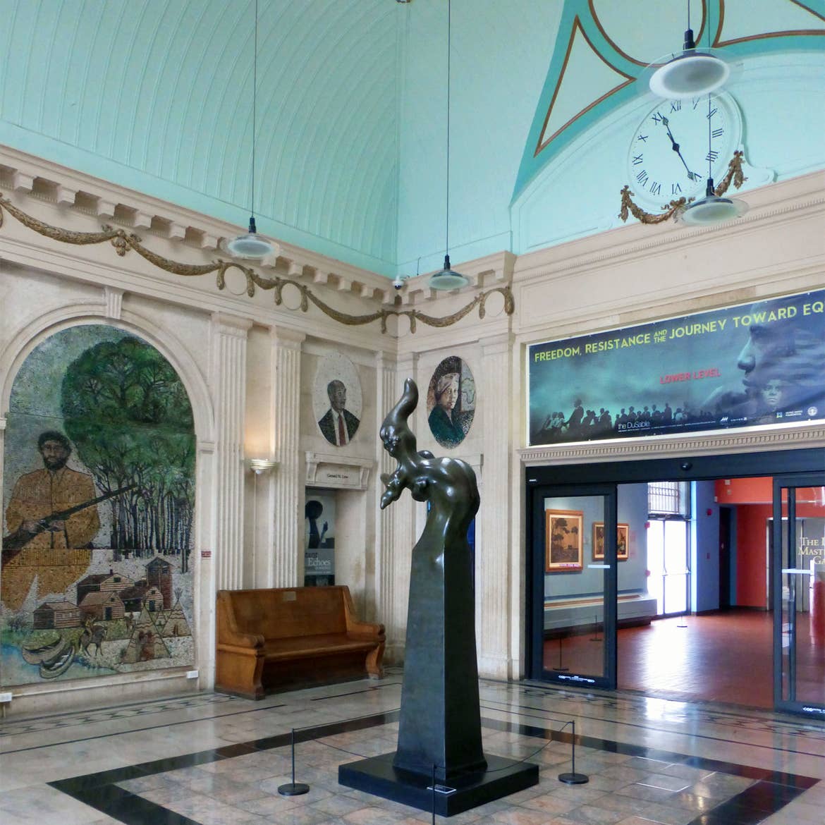 An interior space painted in robins egg blue and ornate decorative moldings have various murals and an abstract, black statue on display.