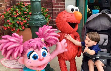 Dakota, Theresa's son, reaches from his stroller to embrace Elmo and Abby Cadabby outside Sesame Street Land.