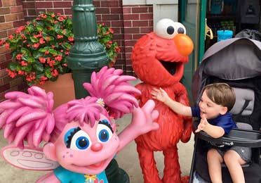 Dakota, Theresa's son, reaches from his stroller to embrace Elmo and Abby Cadabby outside Sesame Street Land.