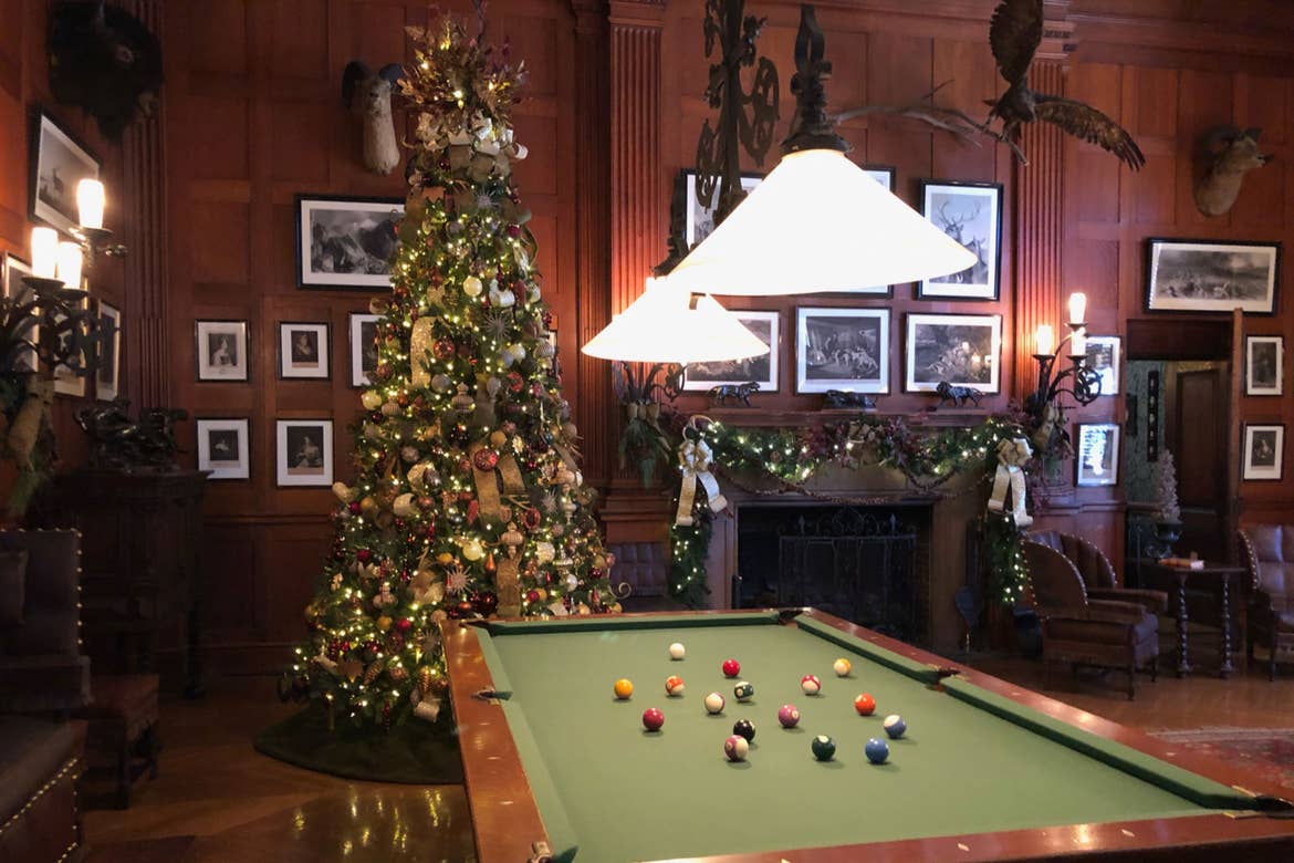 The Recreation Room of the Biltmore Estate with an elaborate fireplace and surrounded by red seating and Christmas trees with a pool table.