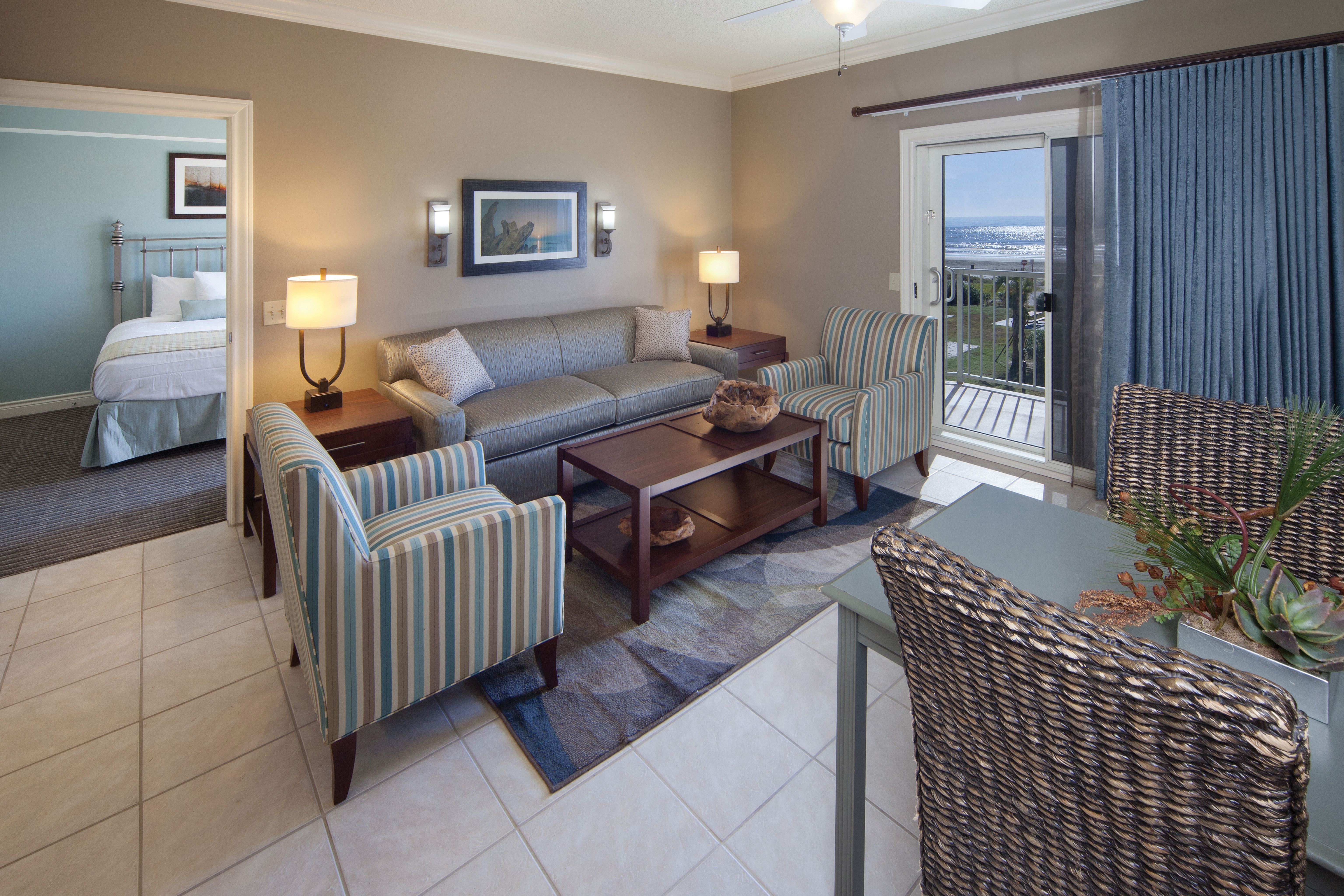 Living room with couch, two accent chairs, and access to balcony in a two-bedroom villa at Galveston Beach Resort