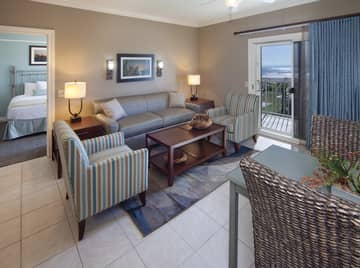 Living room with couch, two accent chairs, and access to balcony in a two-bedroom villa at Galveston Beach Resort