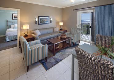 Living room with couch, two accent chairs, and access to balcony in a two-bedroom villa at Galveston Beach Resort