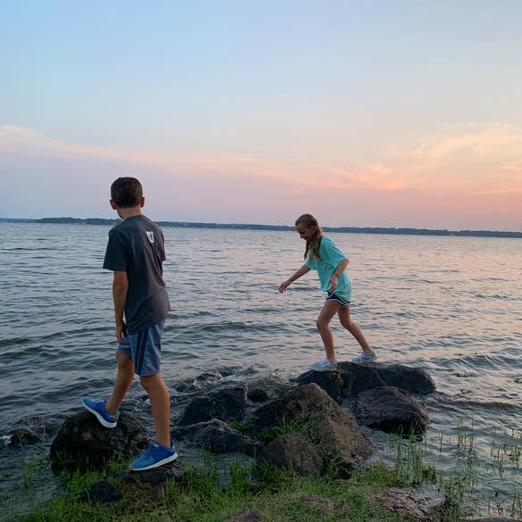 A caucasian boy (left) and girl) climb rocks near the Lake Palestine lakefront.