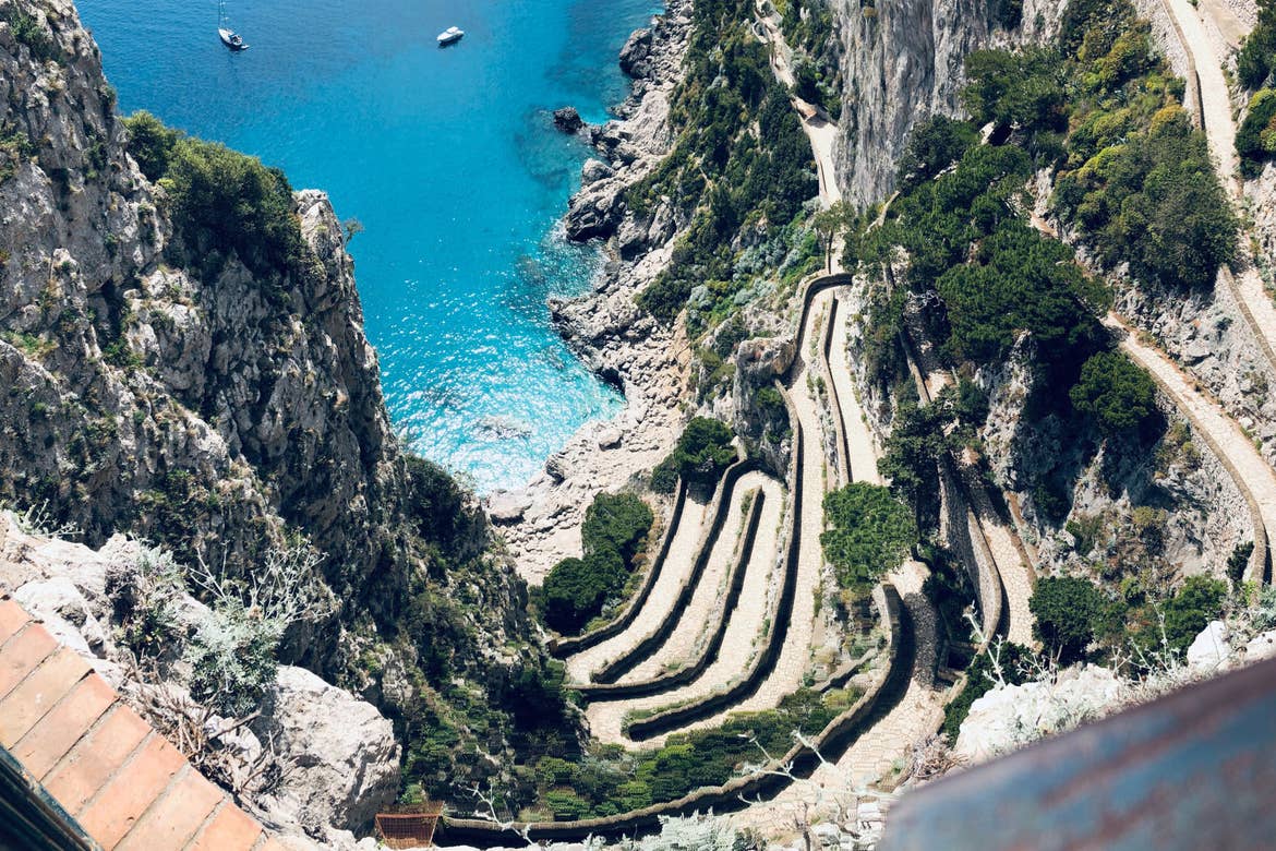 The cliffside of the Capri mountains with winding roads and trees lining the road above the ocean.
