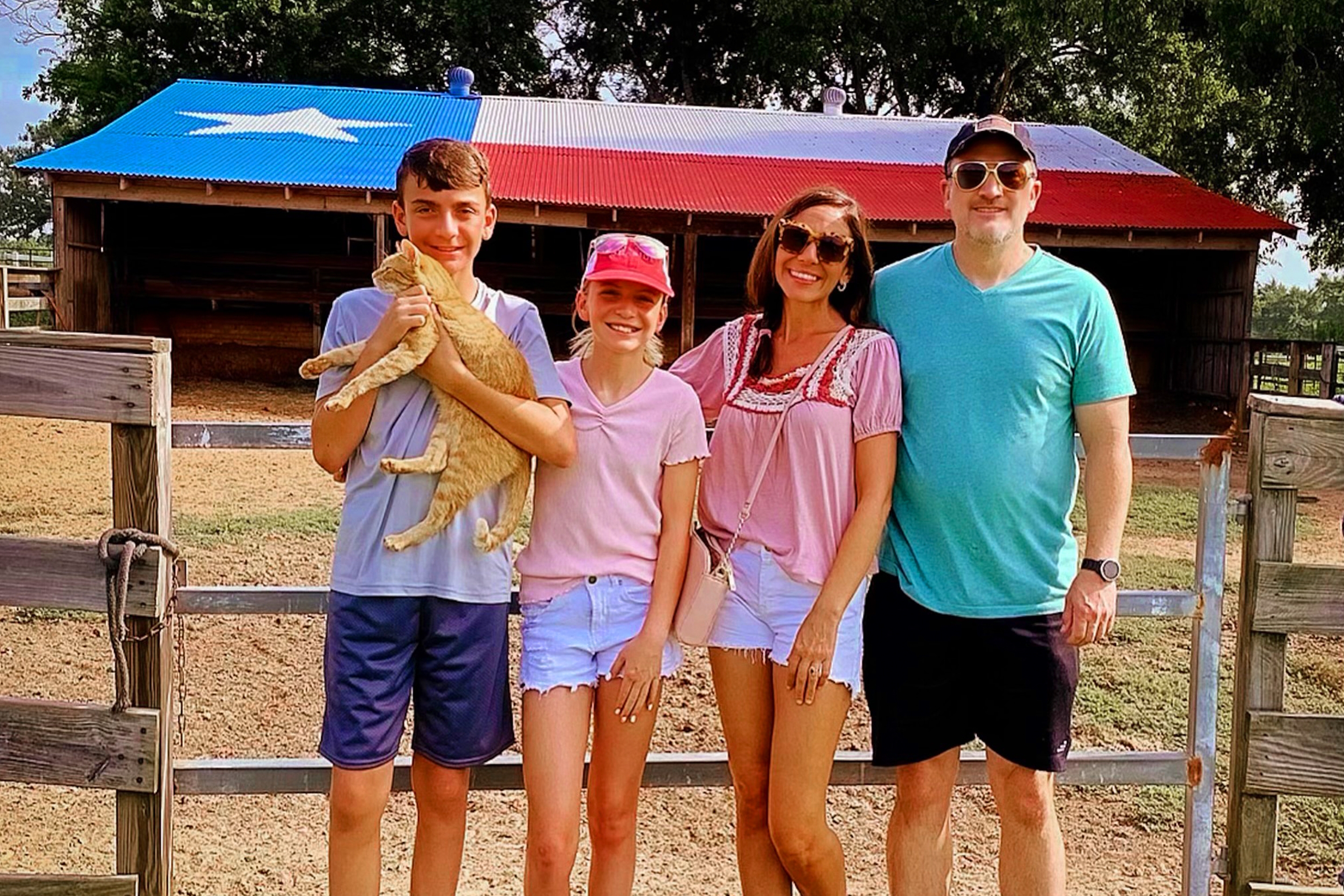 A caucasian family of four stand near a horse stable.