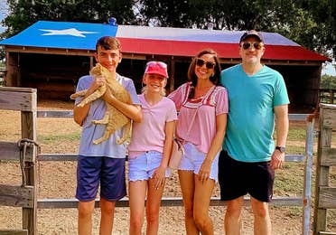 A caucasian family of four stand near a horse stable.
