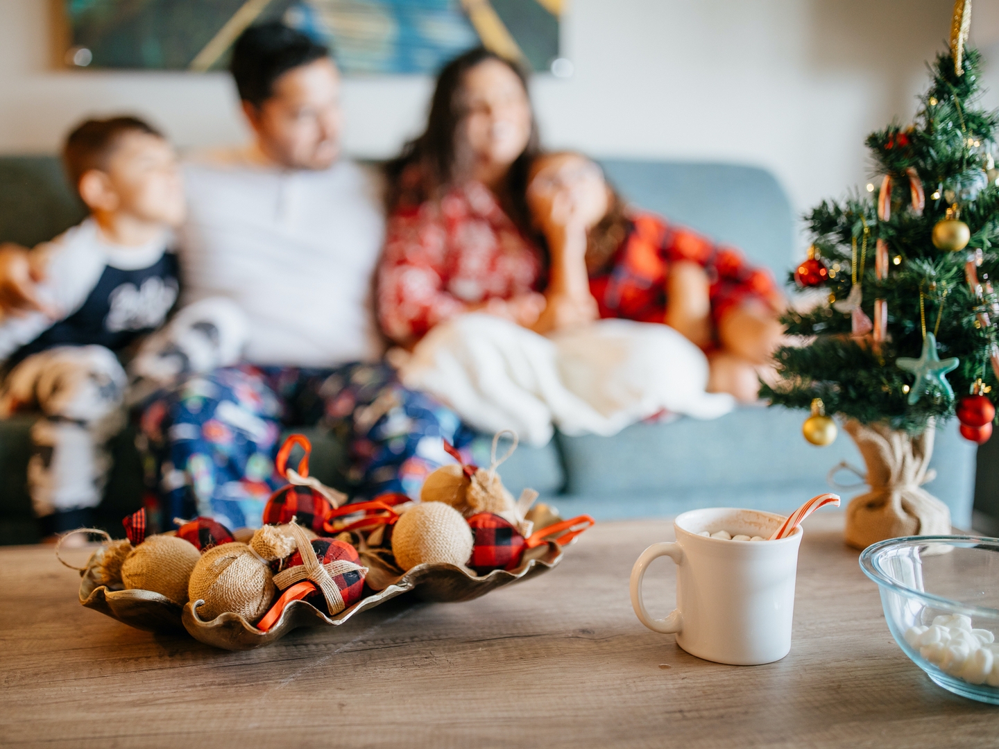 Family of four sitting on couch with view of coffee table with hot chocolate and mini Christmas tree at Orange Lake Resort near Orlando, FL.