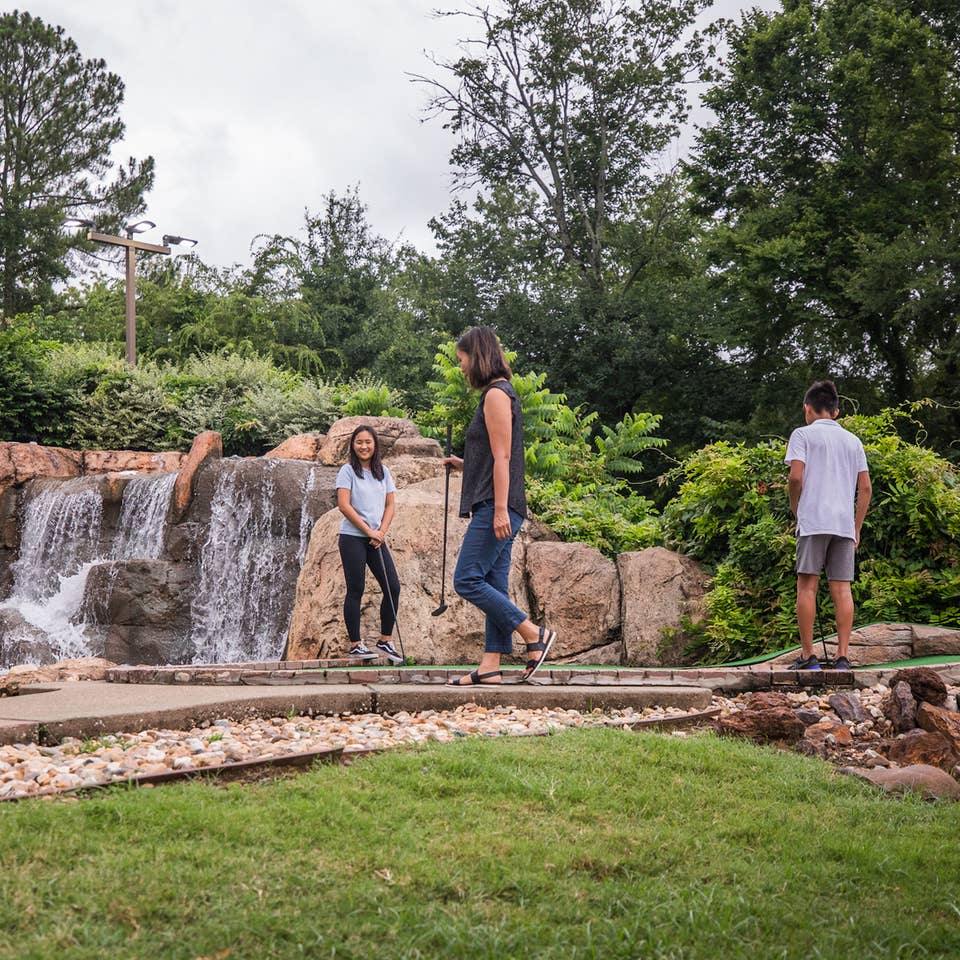 Three guests playing mini golf in front of waterfall at Villages Resort in Flint, Texas.