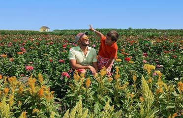 A young boy and man sit in the middle of a wildflower field.