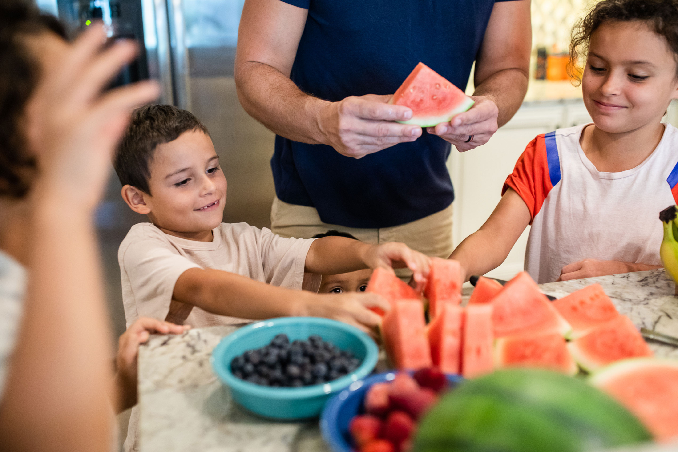 Brenda's husband, Isaiah, preps tasty fruits at the kitchen countertop with his sons watching.