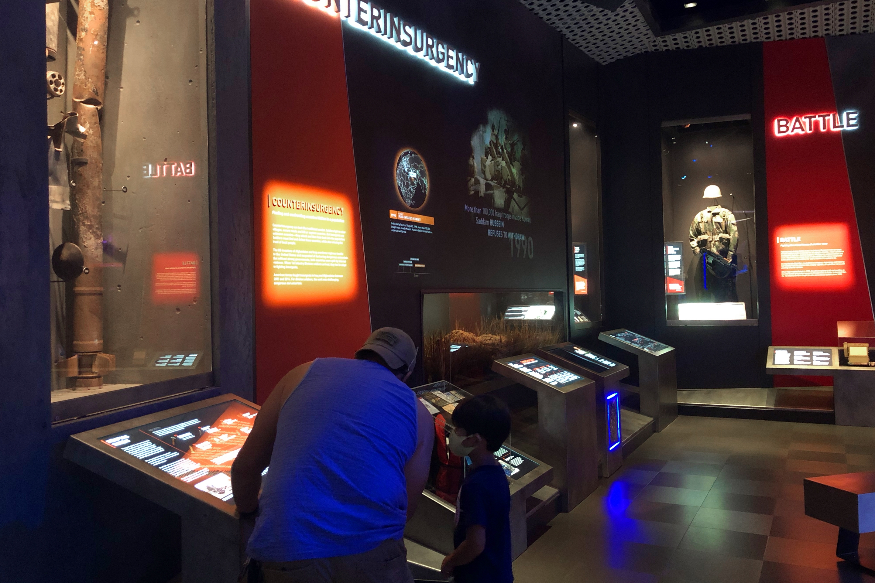 A man and child look at various war artifacts in an exhibit.