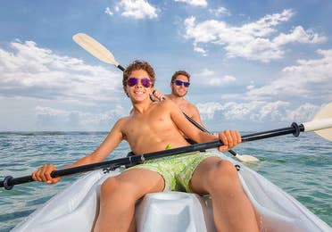 Father and son, smiling and wearing sunglasses while kayaking on the ocean at The Royal Haciendas in Playa del Carmen, Mexico