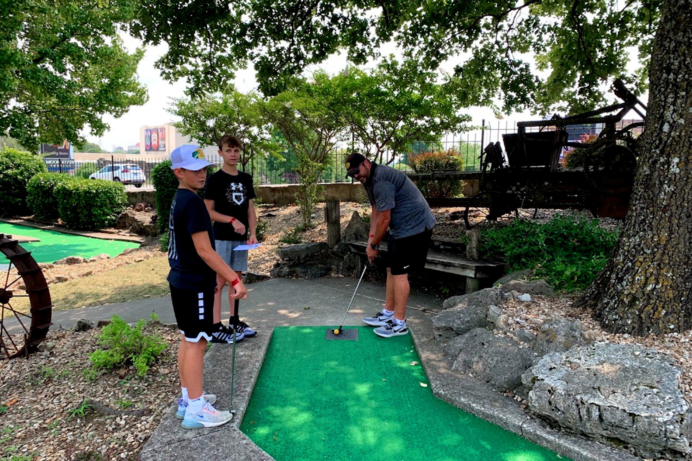 Two boys and a man play a round of mini golf on a course.