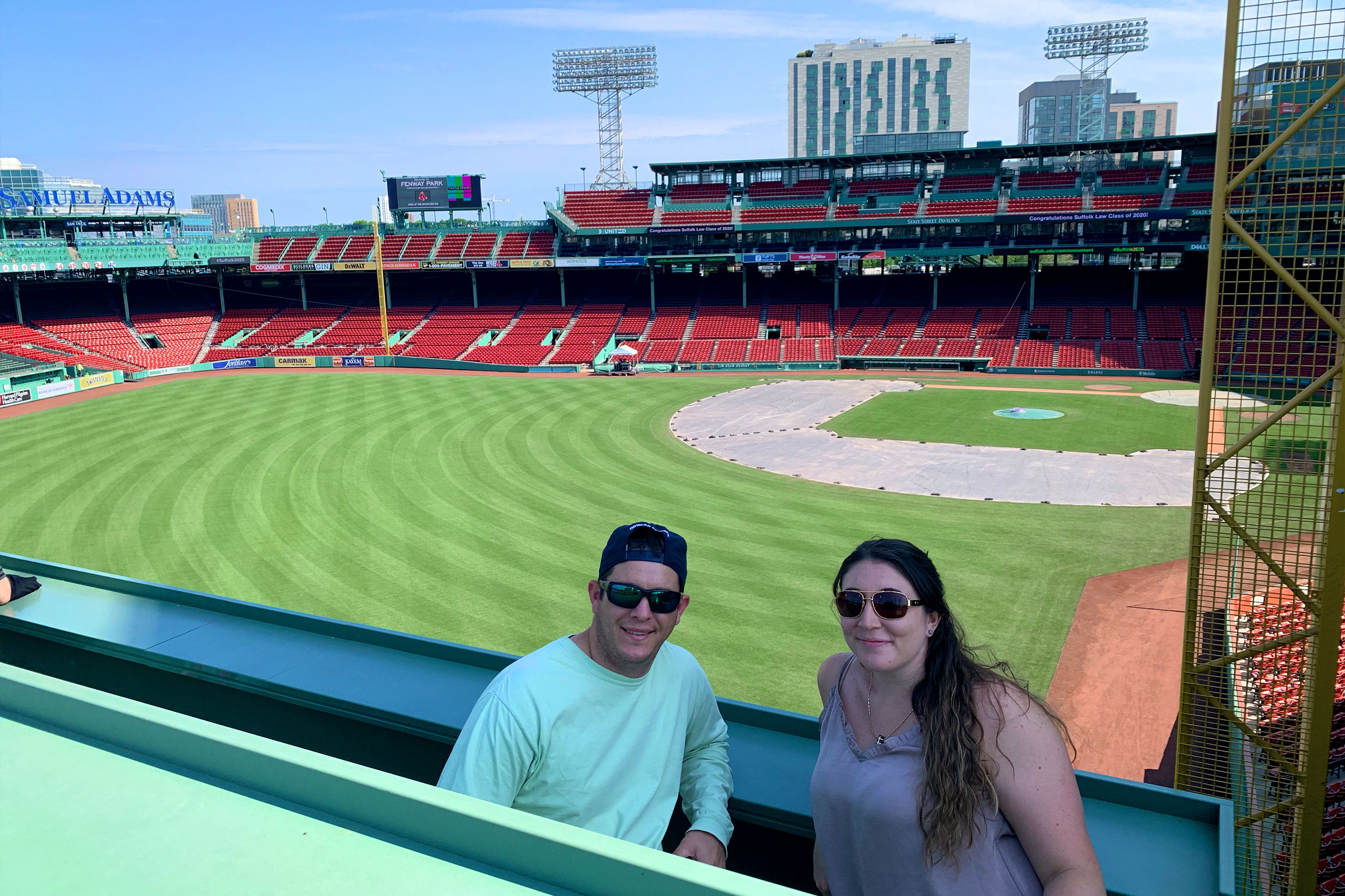 A man (left) and woman (right) standing from the 'Green Monster' overlooking Fenway Park.