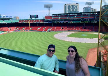 A man (left) and woman (right) standing from the 'Green Monster' overlooking Fenway Park.