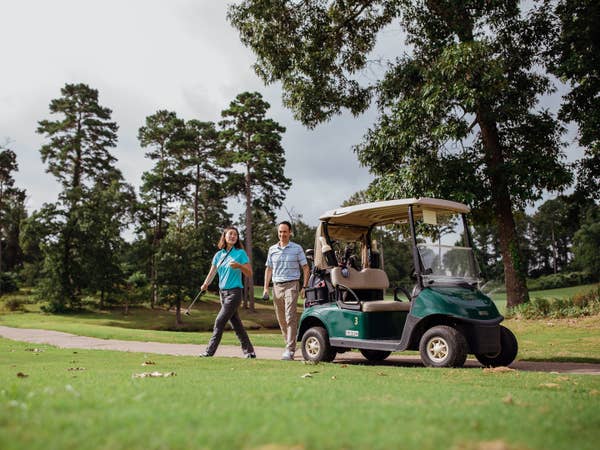 Couple standing next to golf cart on golf course at Eagle's Bluff Country Club near Villages Resort in Flint, Texas.