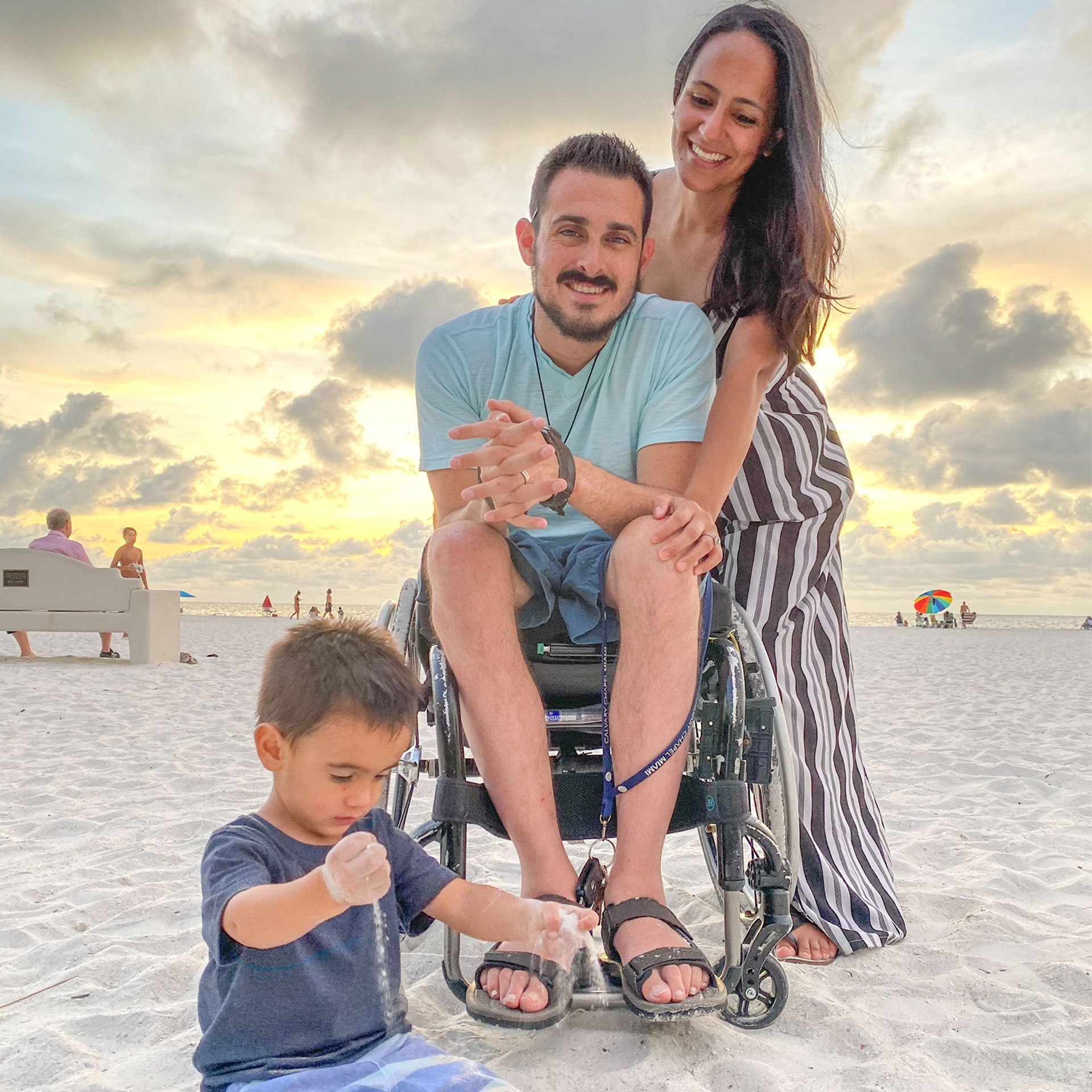 Author, Danny Pitaluga (middle), his wife, Val (right) and son, Joey (left), pose on a white sandy beach with a cloudy sunset behind them.