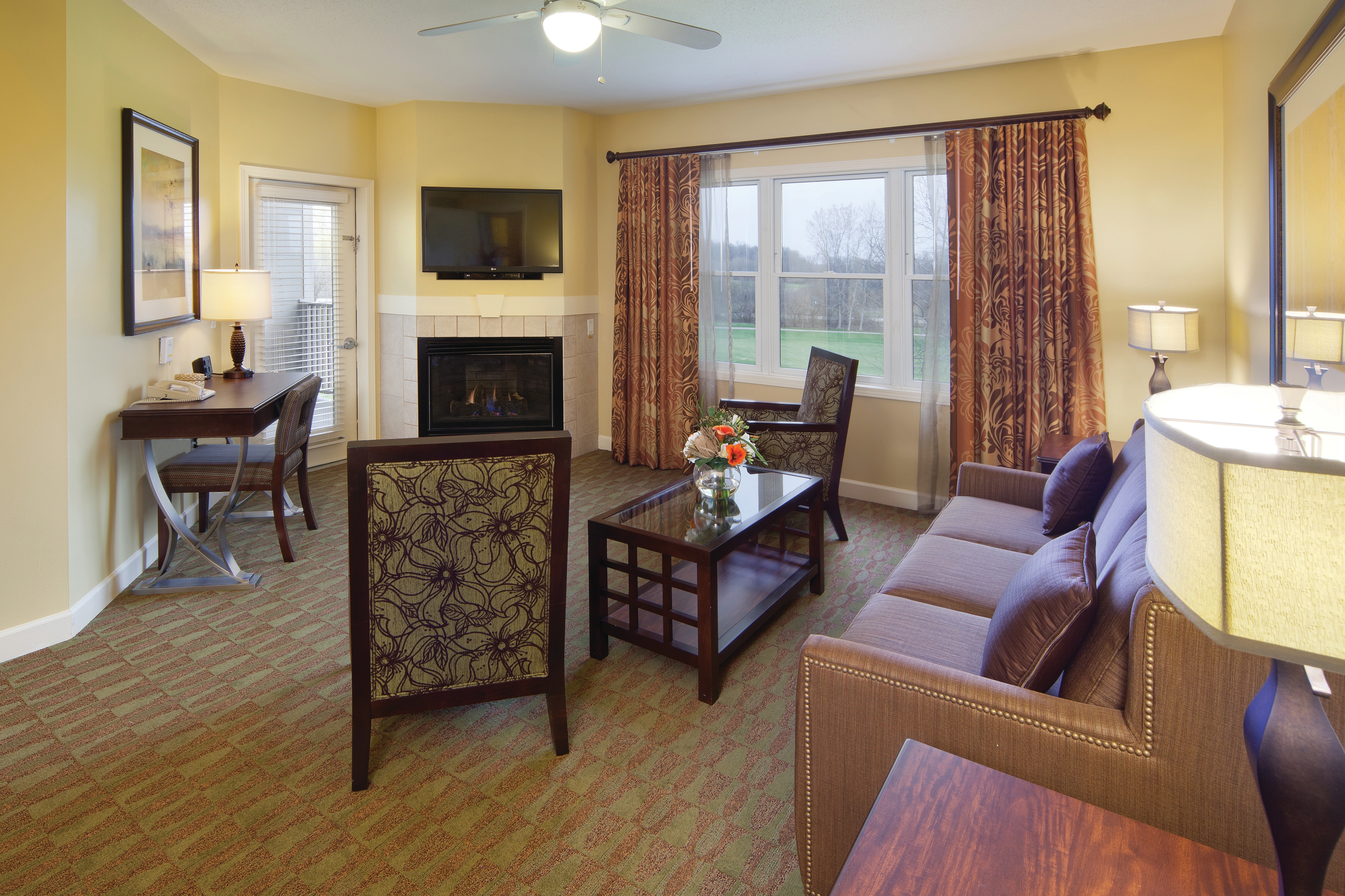 Living room with couch, two accent chairs, fireplace and flat screen TV in a one-bedroom villa at Lake Geneva Resort